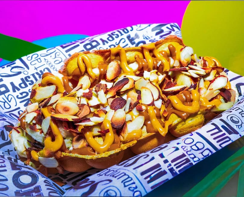 A waffle topped with sliced almonds, banana, and drizzled with peanut butter and caramel sauce.