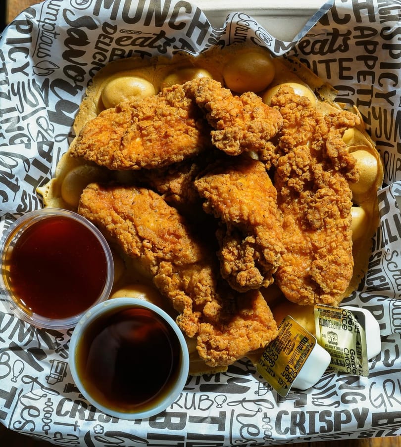 Crispy fried chicken tenders on a bubble waffle with syrup, hot sauce, and butter.
