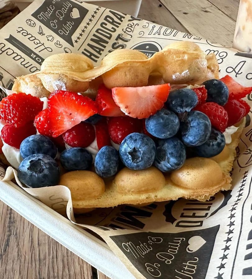 A bubble waffle filled with whipped cream, fresh strawberries, blueberries, and raspberries.